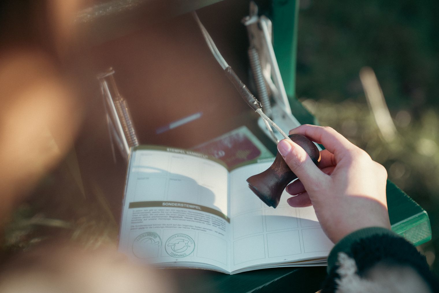 Hand setzt Stempel der Harzer Wandernadel in den Wanderpass.