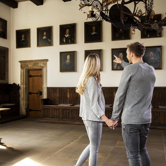 Ein Paar betrachtet Porträts im historischen Friedenssaal des Osnabrücker Rathauses.