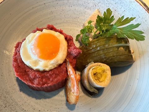 Labskaus mit Spiegelei, Gewürzgurke und Rollmops auf Keramikteller, appetitlich angerichtet.