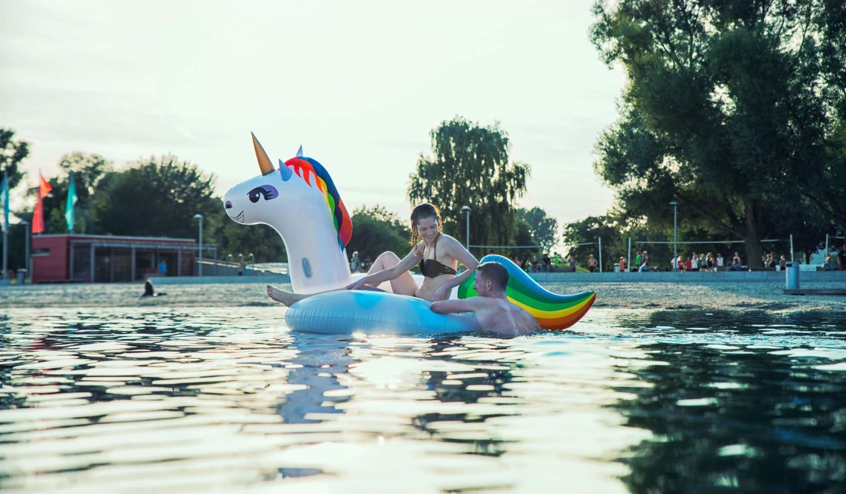 Een jonge vrouw en een jonge man baden in de Allersee met een opblaasbare eenhoorn, © Wolfsburg AG / Jenko Sternberg